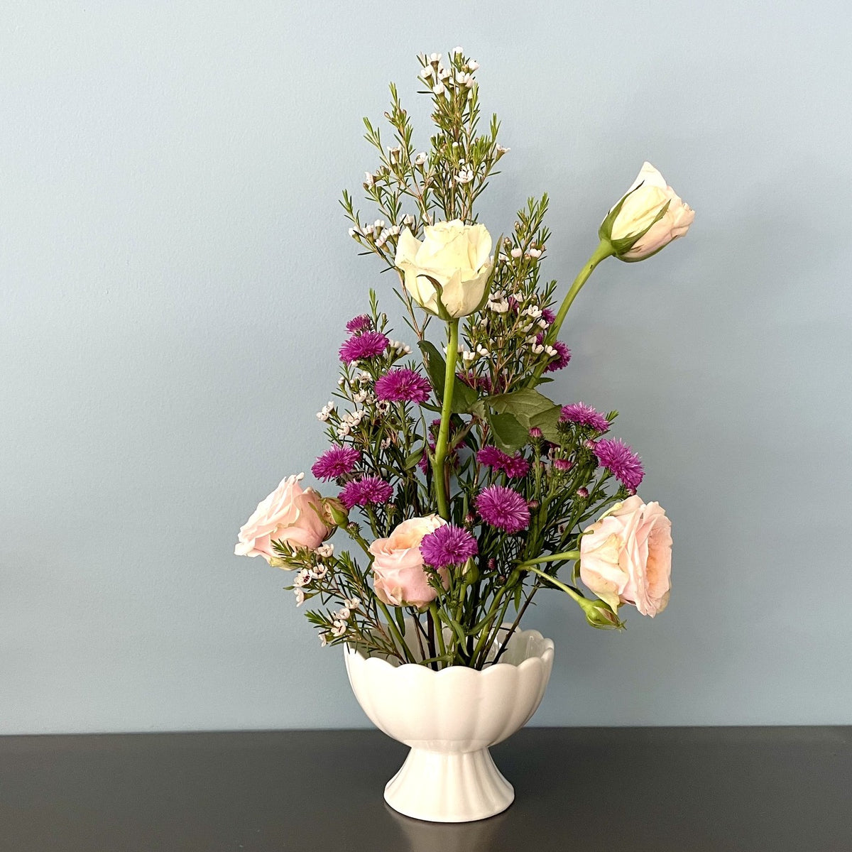 A floral arrangement in a white pedestal vase.   Vase has flower frog pin for dramatic styling using fewer stems.   Great for kitchen counters, bedrooms, living room.   